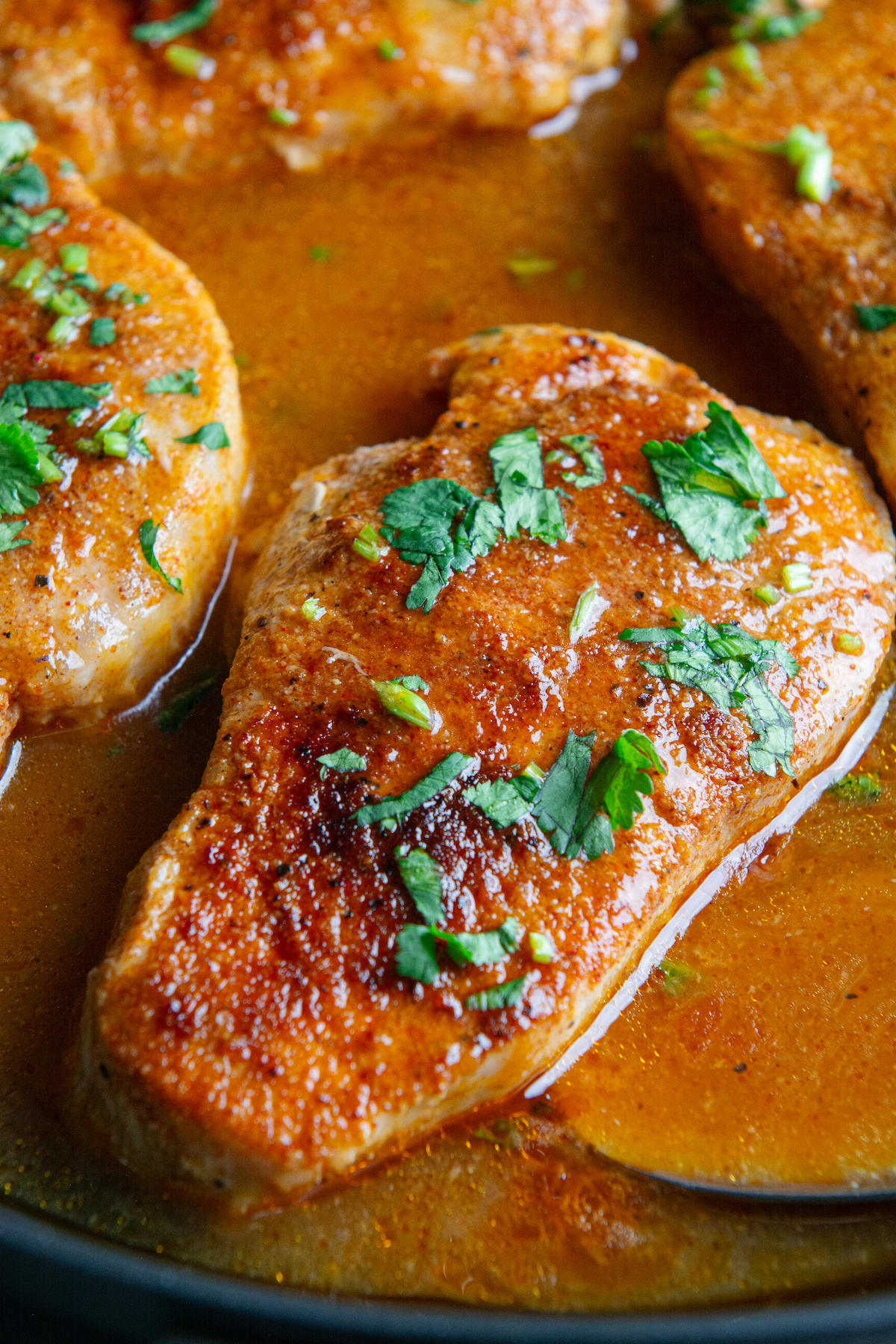 A skillet with pan seared boneless pork chops cooked in a delicious seasoned sauce and sprinkled with cilantro on top.