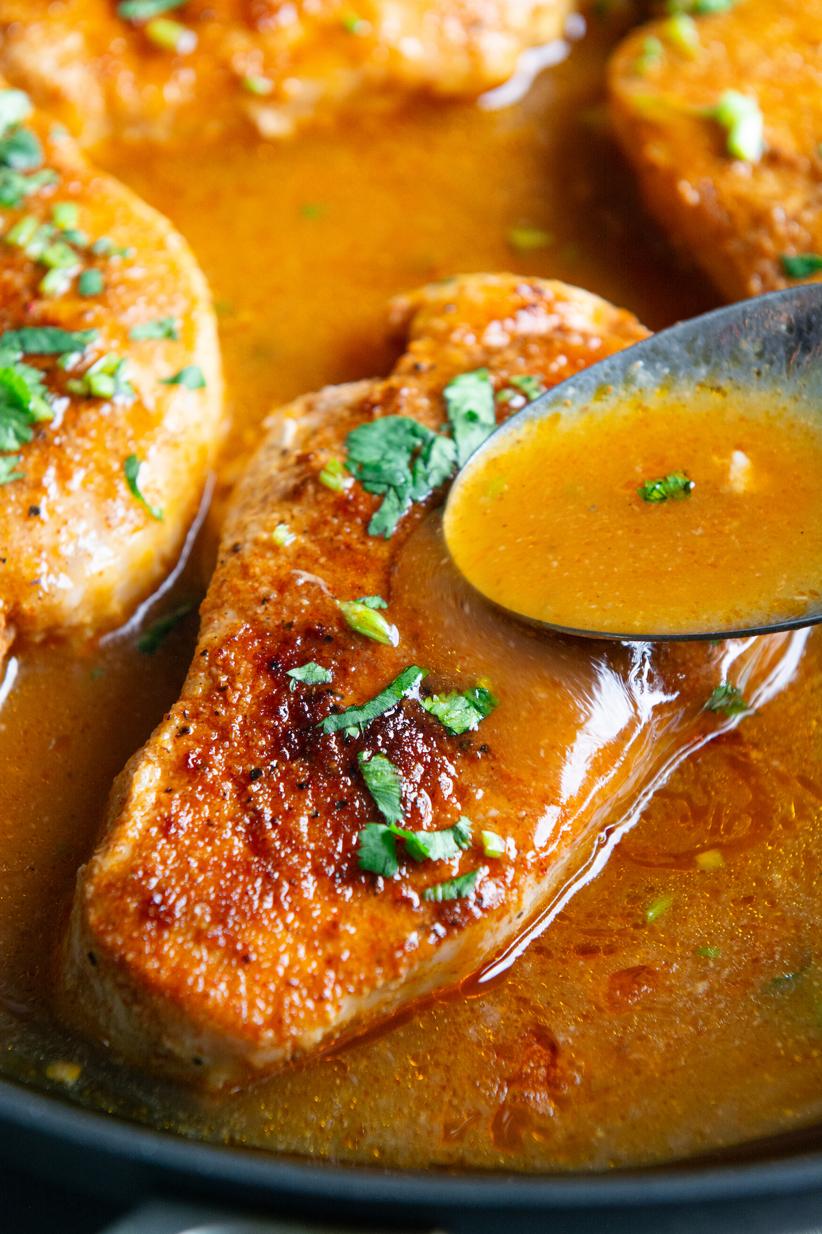 A skillet with pan seared boneless pork chops bathed in a delicious seasoned sauce and sprinkled with cilantro on top.