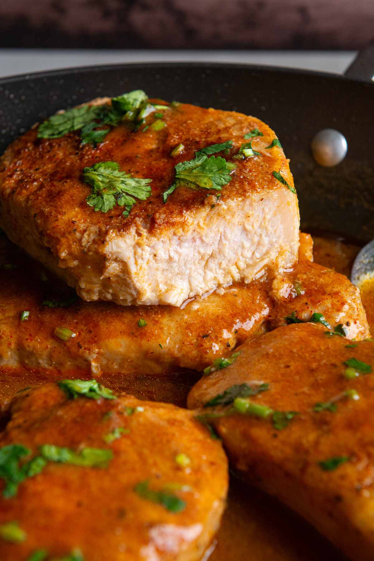 A skillet with pan seared boneless pork chops cooked in a delicious seasoned sauce and sprinkled with cilantro on top.