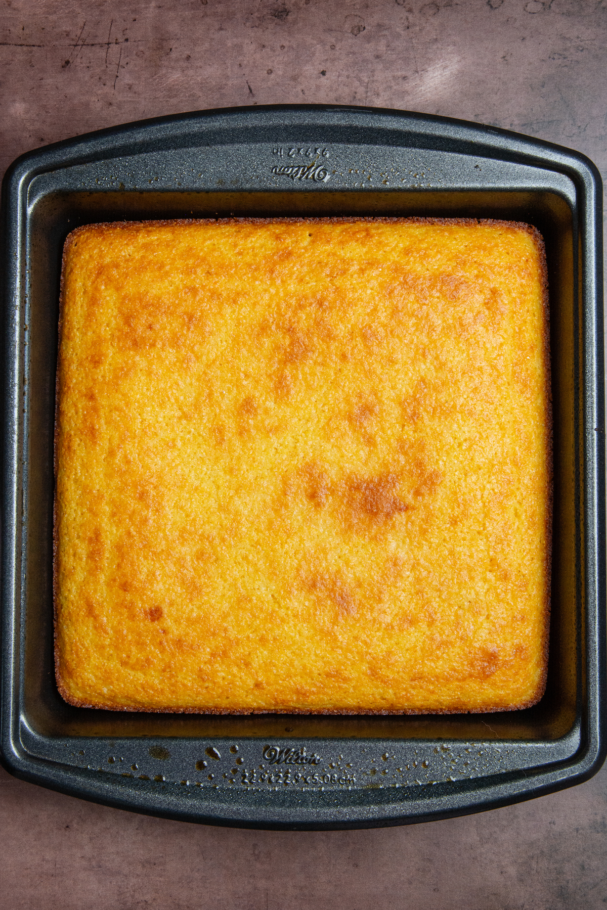 A golden brown baked cornbread in an 8x8 baking pan.