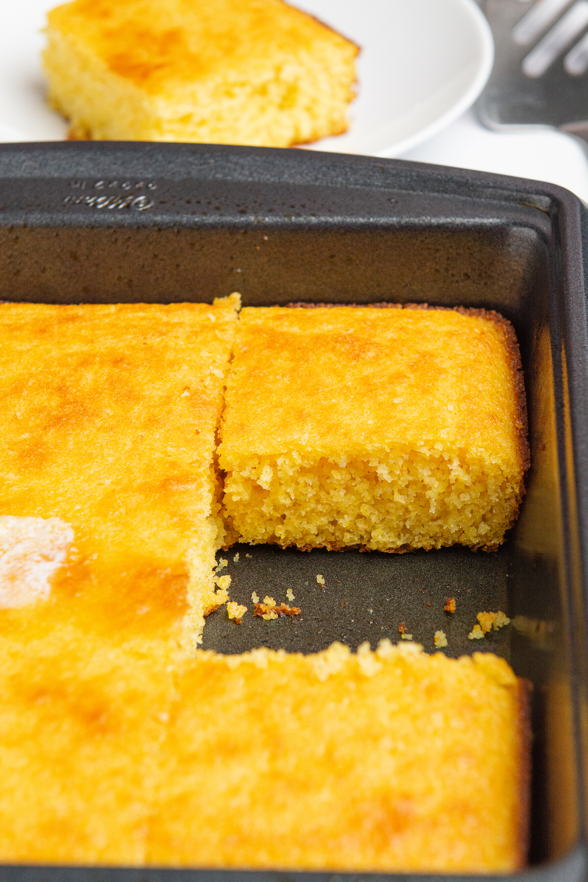 A golden brown baked cornbread in baking pan cut into squares.