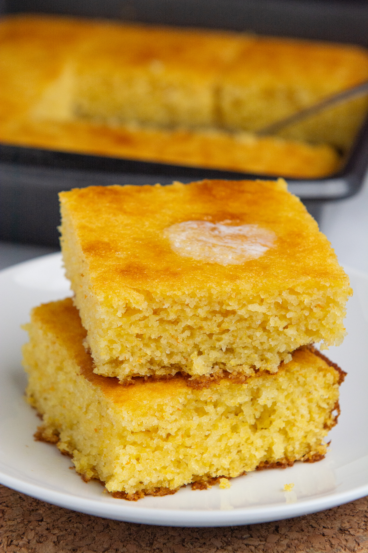 Two squares of golden brown cornbread stacked on top of each other with melting butter on top.