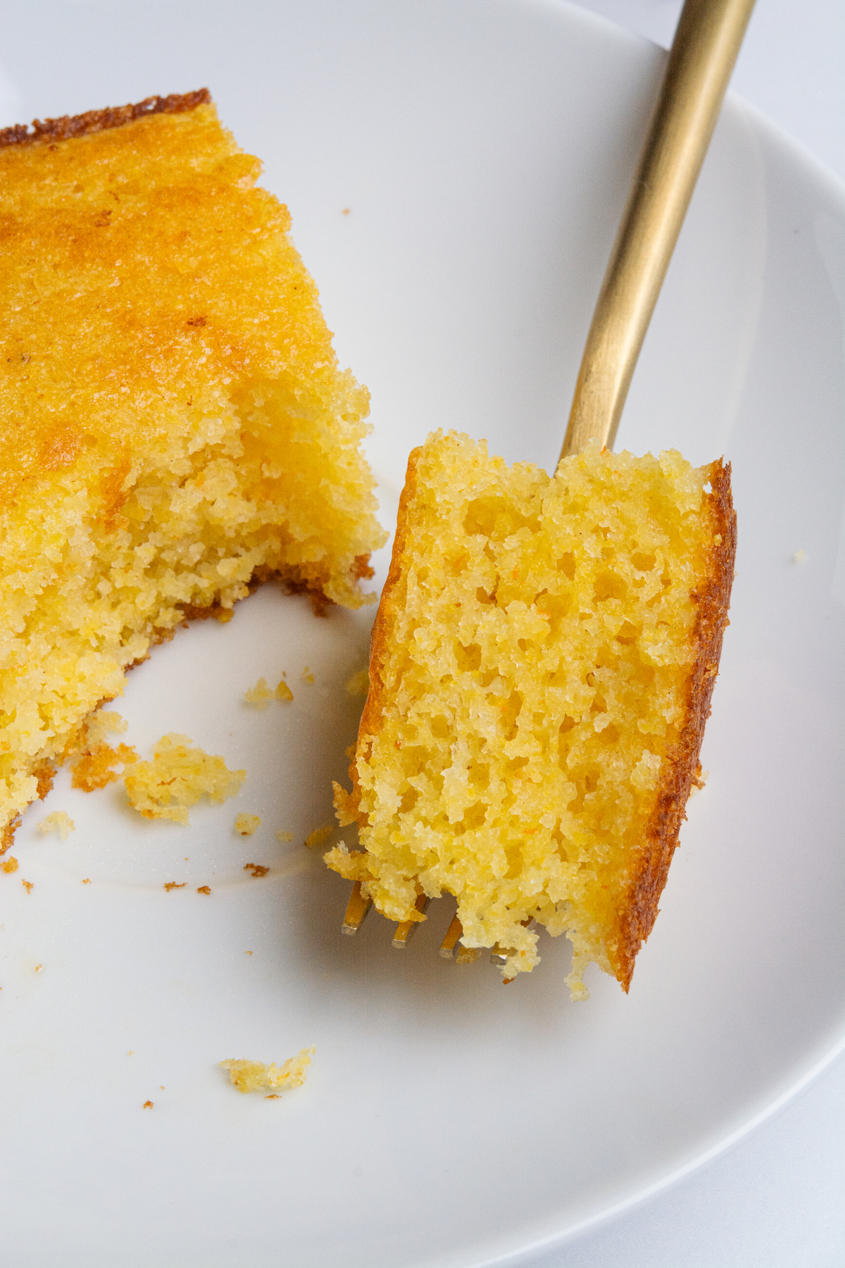 A fork holding a bite-sized piece of a soft, buttery, golden brown cornbread.