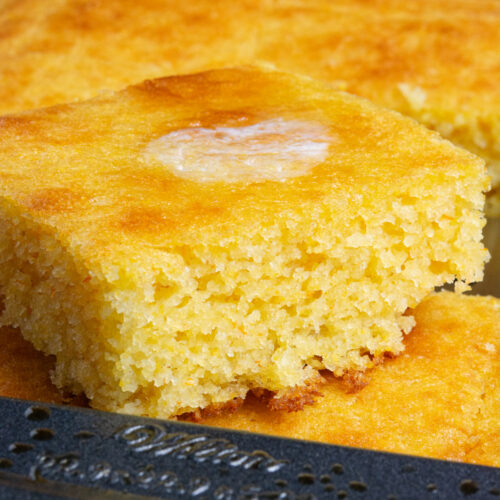 A square of golden brown cornbread with melted butter on top.