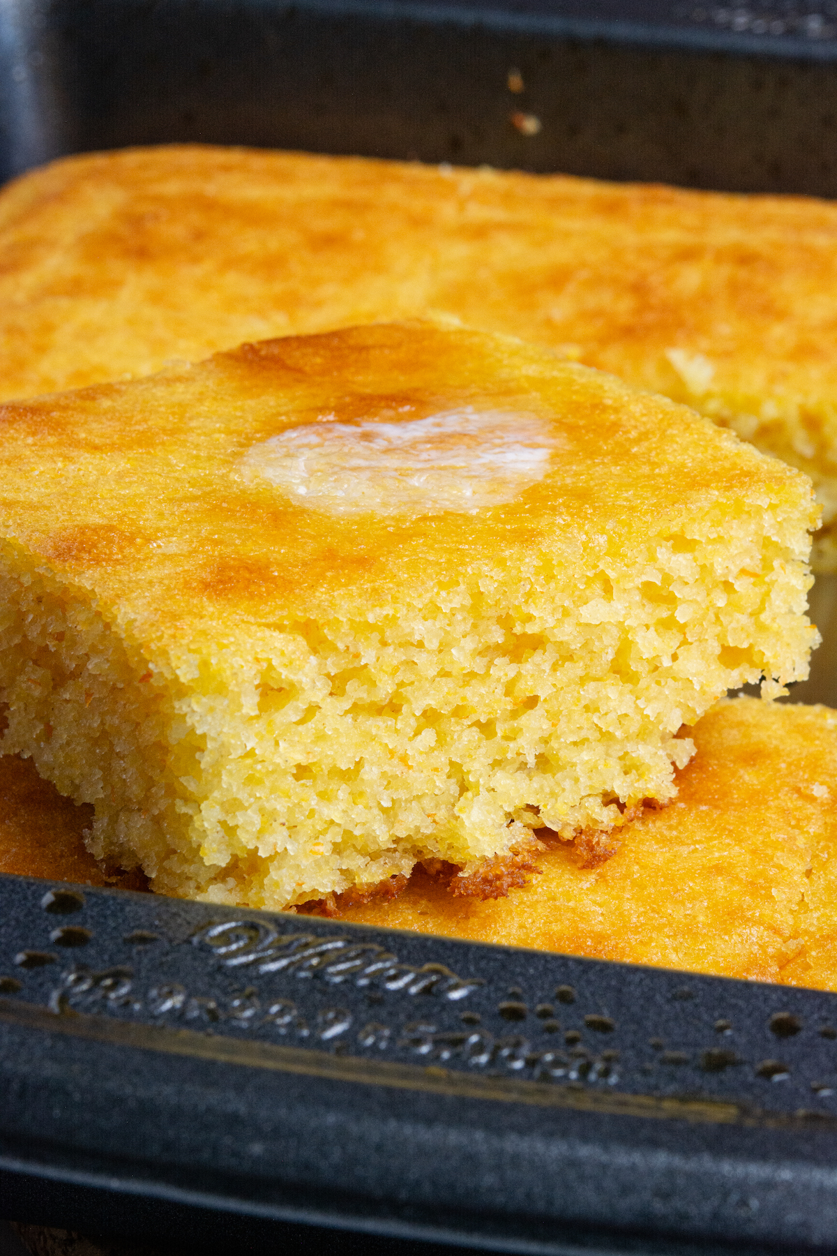 A square of golden brown cornbread with melted butter on top.