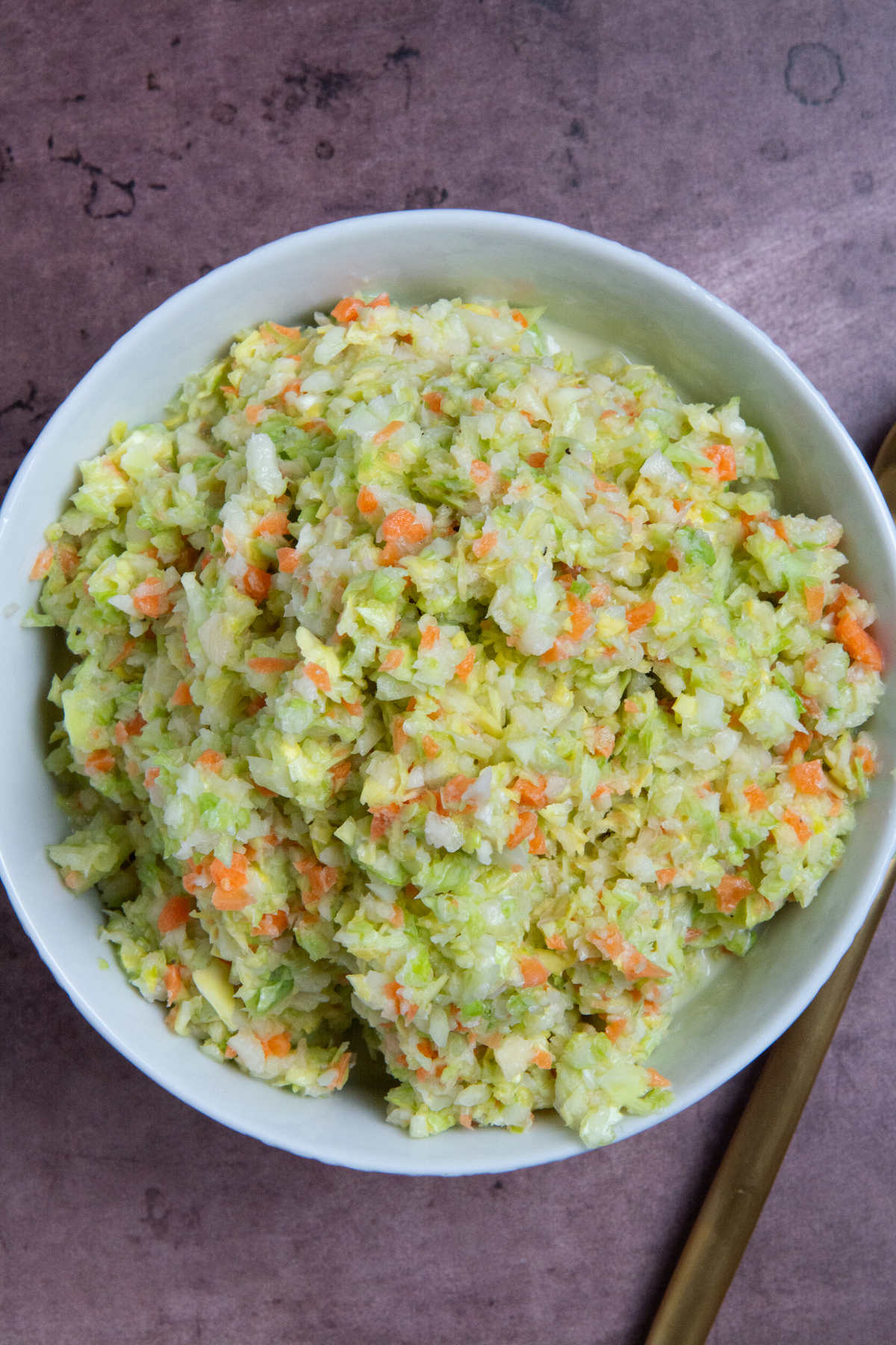 A bowl with a copycat KFC coleslaw made with chopped green cabbage and carrot, tossed in a sweet and tangy buttermilk dressing.