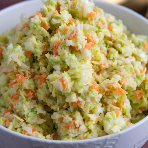 A bowl with a copycat KFC coleslaw made with chopped green cabbage and carrot, tossed in a sweet and tangy buttermilk dressing.