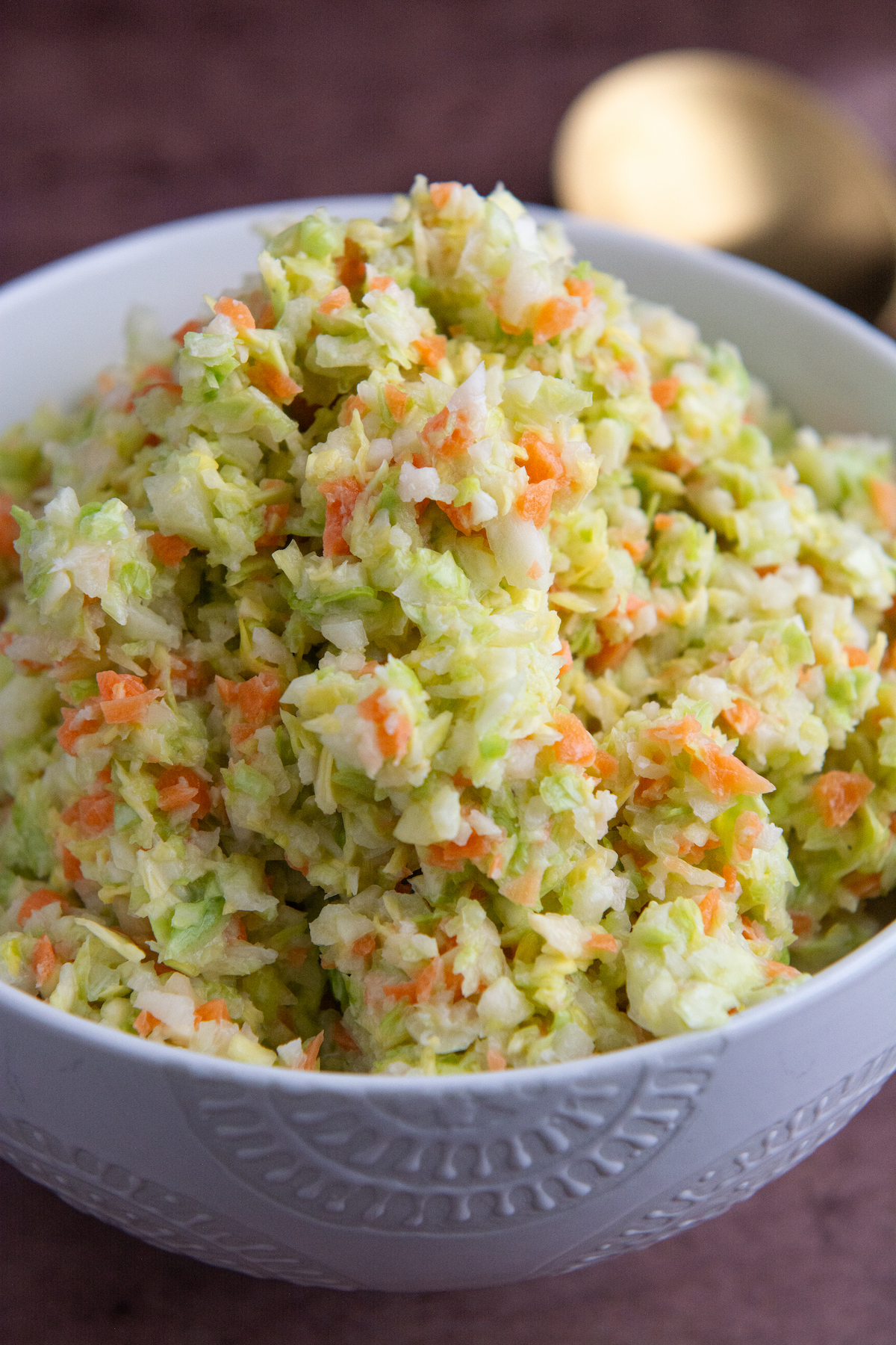 A bowl with a copycat KFC coleslaw made with chopped green cabbage and carrot, tossed in a sweet and tangy buttermilk dressing.