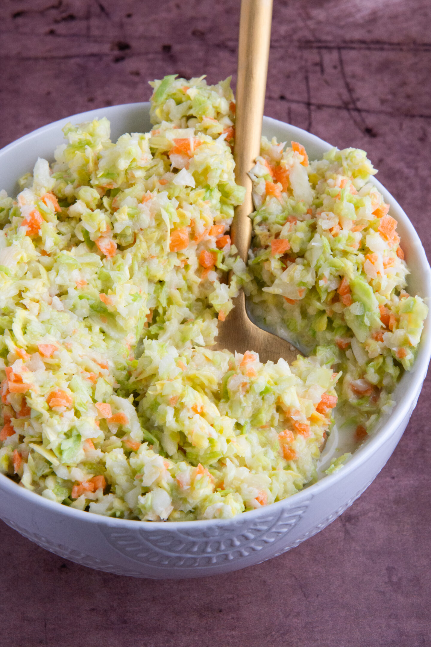 A bowl with a copycat KFC coleslaw made with chopped green cabbage and carrot, tossed in a sweet and tangy buttermilk dressing.