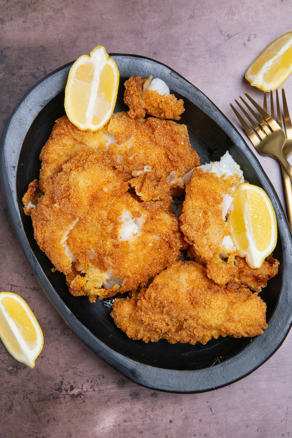 A plate with pieces of crispy fried fish with lemon wedges on the side.