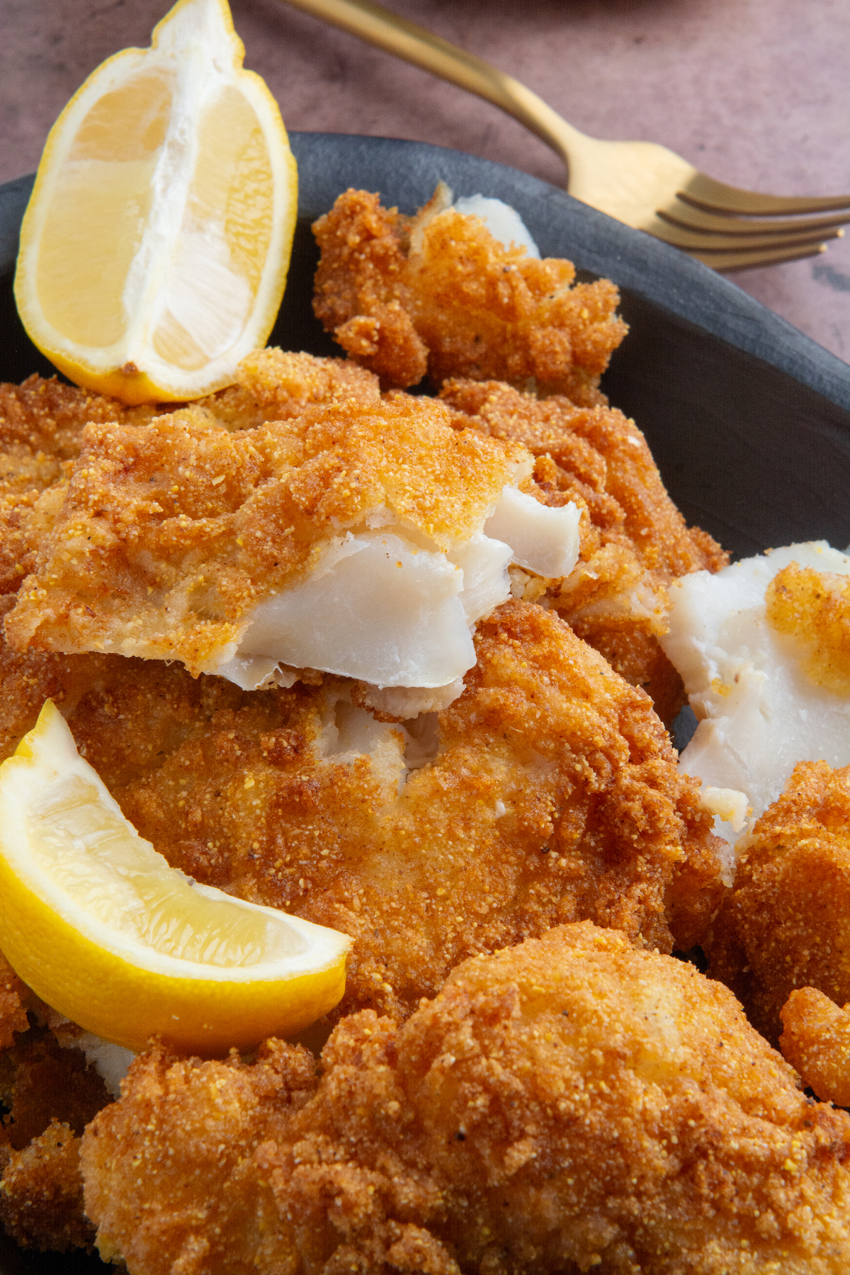 A plate with pieces of crispy fried fish with lemon wedges on the side.