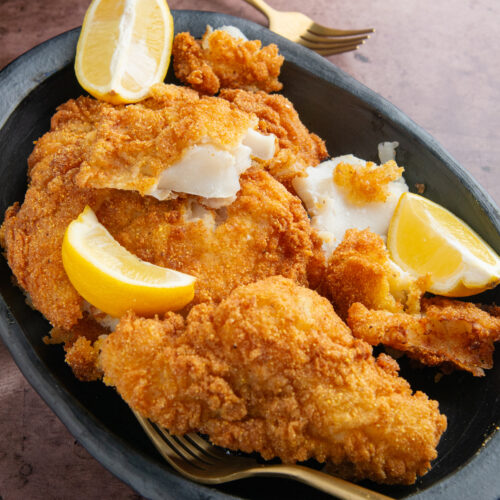 A plate with pieces of crispy fried fish with lemon wedges on the side.