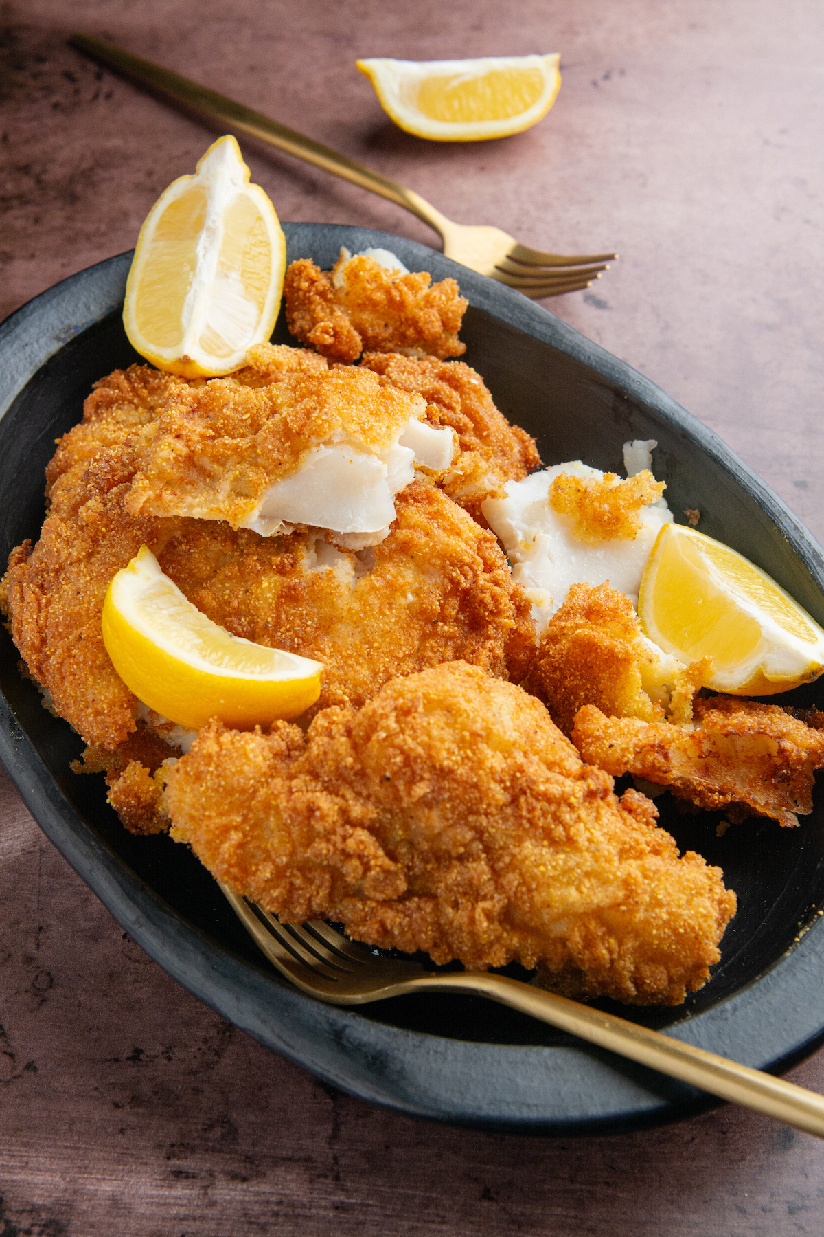 A plate with pieces of crispy fried fish with lemon wedges on the side.