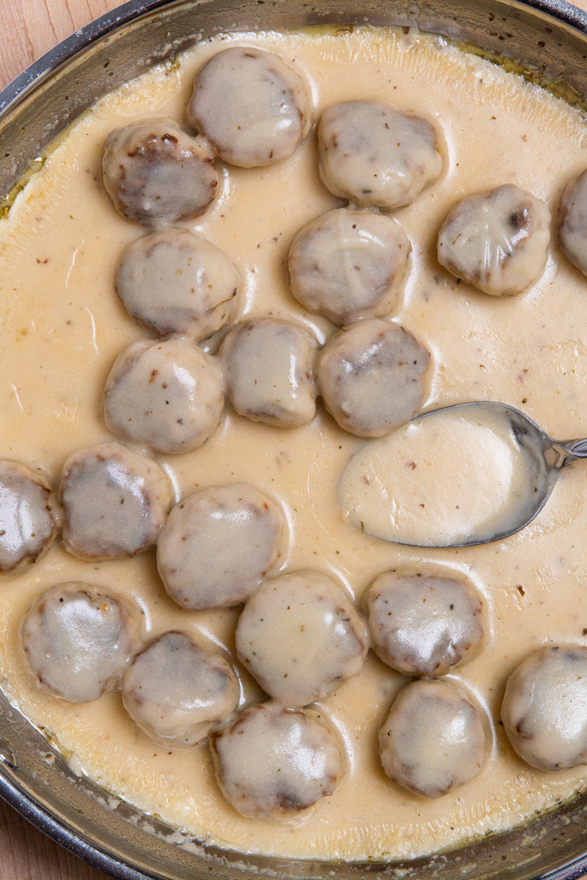 A large pan with cooked chicken meatballs in a creamy sauce.