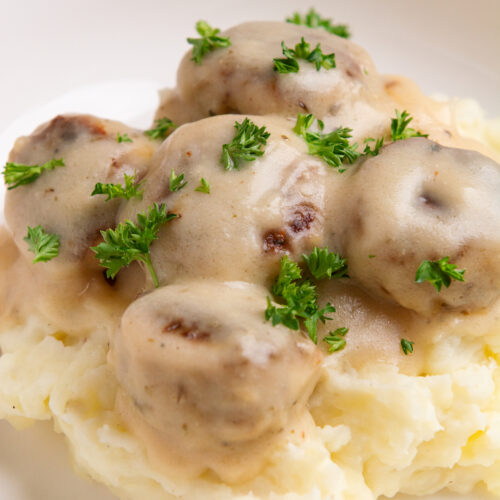 A plate with creamy chicken meatballs resting on a bed of mashed potatoes.