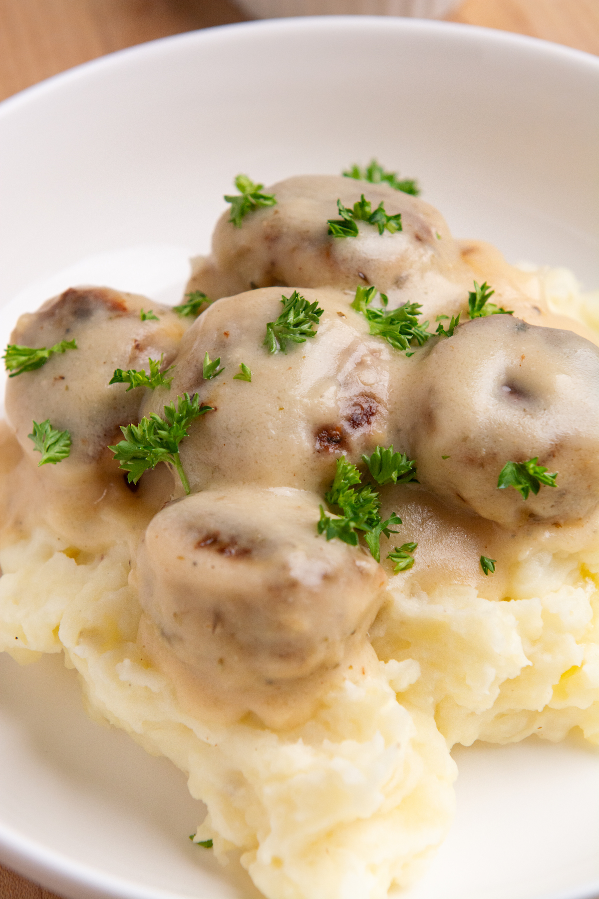 A plate with creamy chicken meatballs resting on a bed of mashed potatoes.