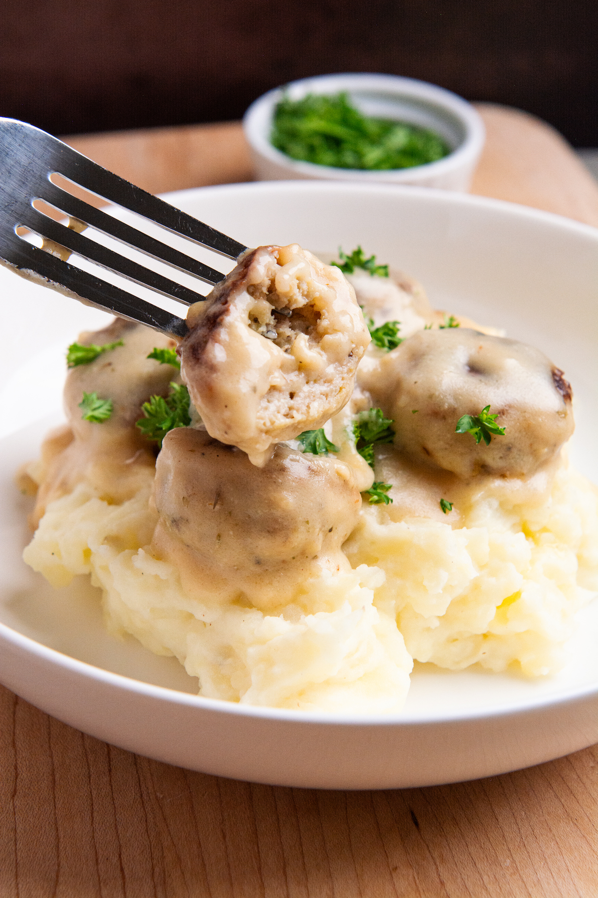 A plate with creamy chicken meatballs resting on a bed of mashed potatoes.