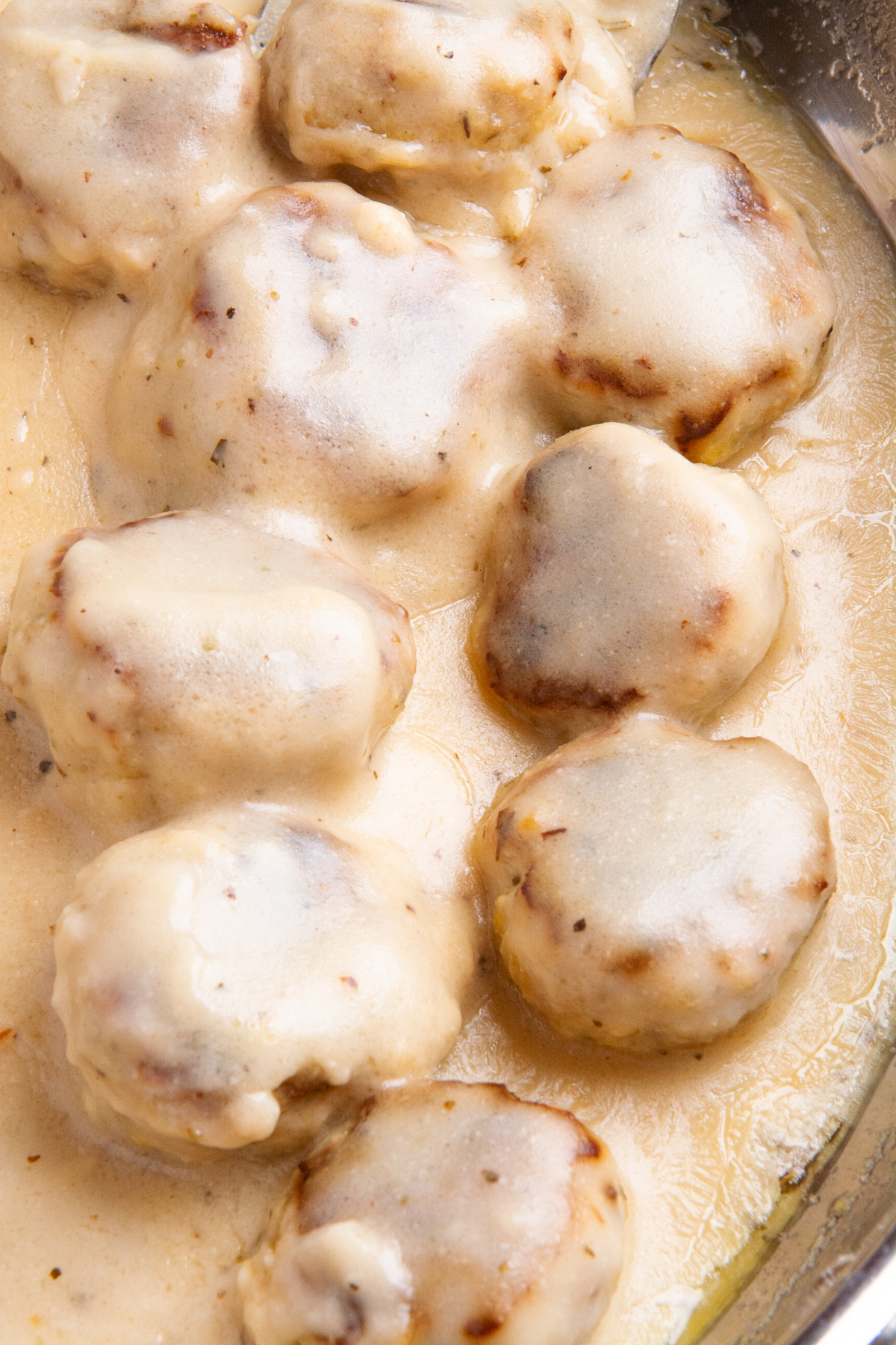 A large pan with cooked chicken meatballs in a creamy sauce.