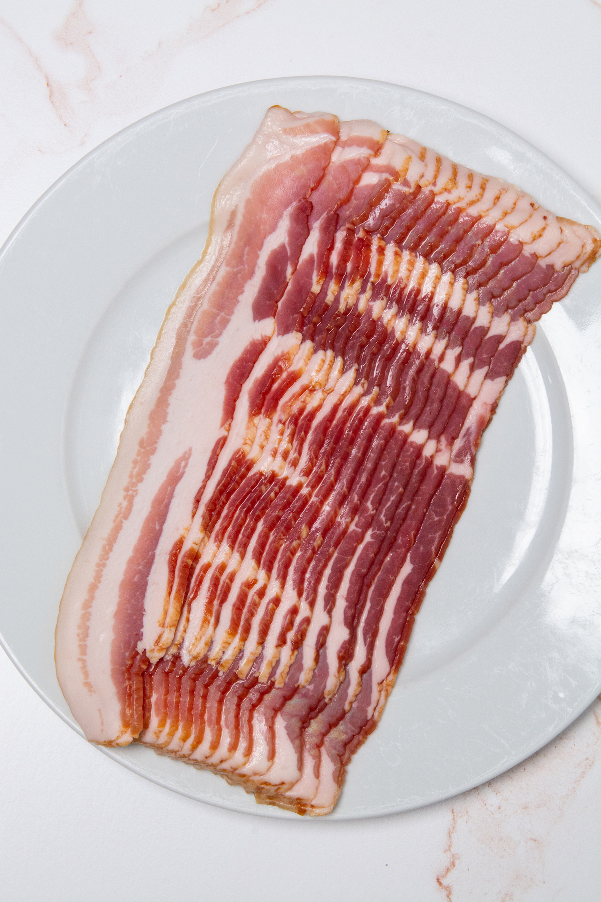 A plate with uncooked strips of bacon.