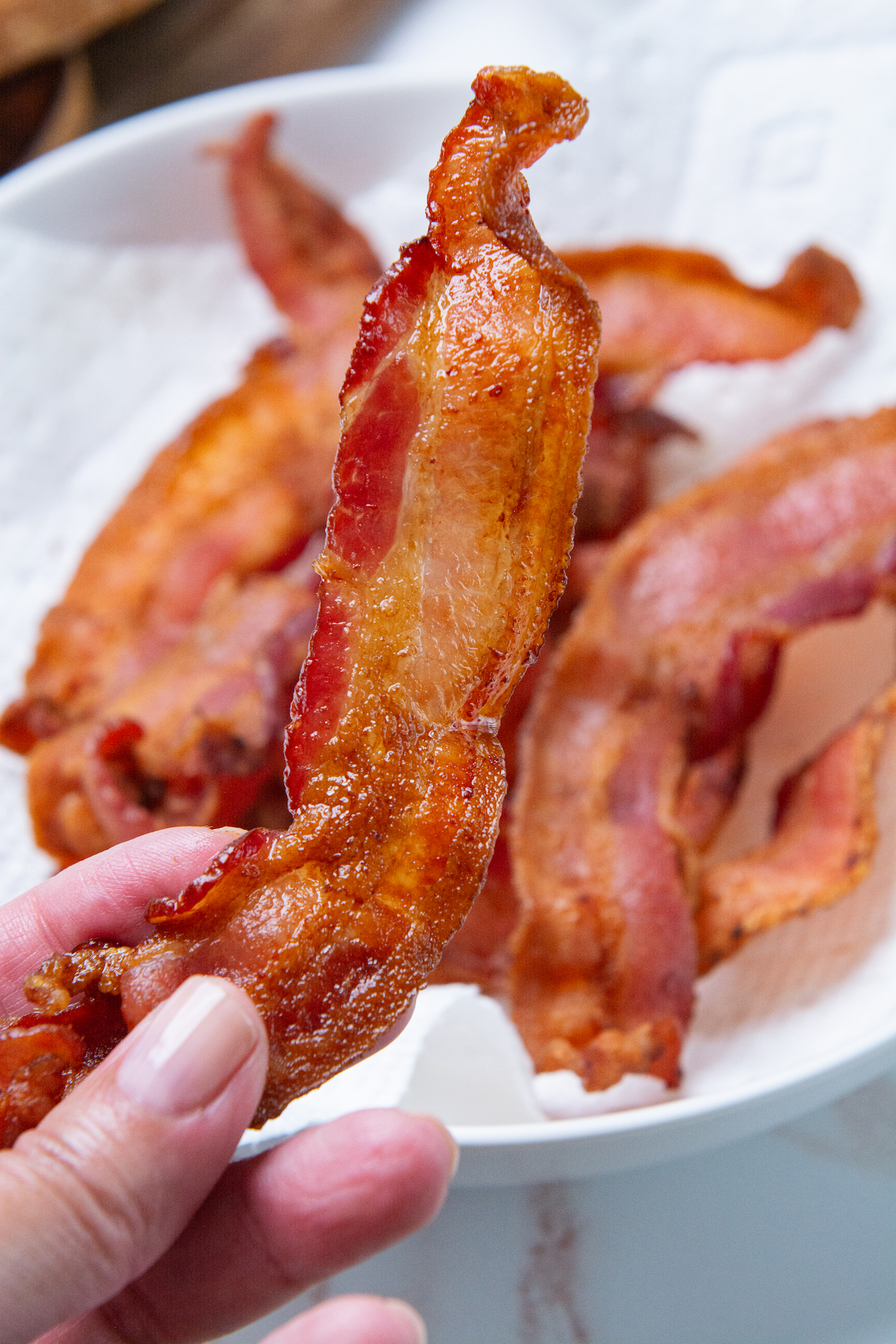 A hand holding a strip of crispy air fryer bacon.