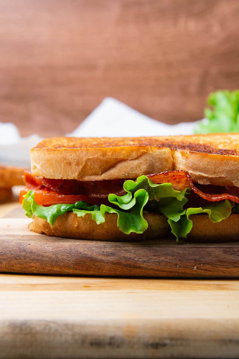 A BLT sandwich resting on a wooden cutting board.