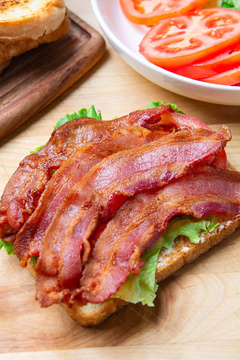 A BLT sandwich without the top slice of bread resting on a wooden cutting board.