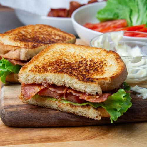 A BLT sandwich cut in half resting on a wooden cutting board.
