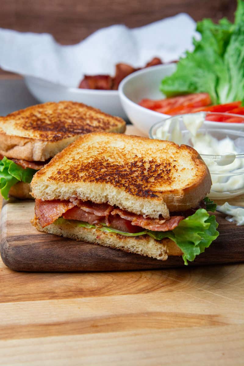 A BLT sandwich cut in half resting on a wooden cutting board.