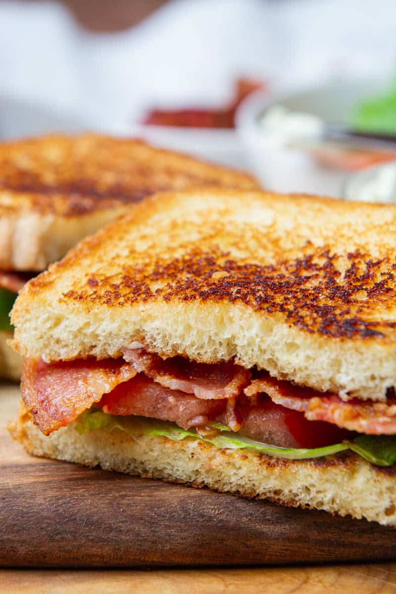 half of a BLT sandwich resting on a wooden cutting board.