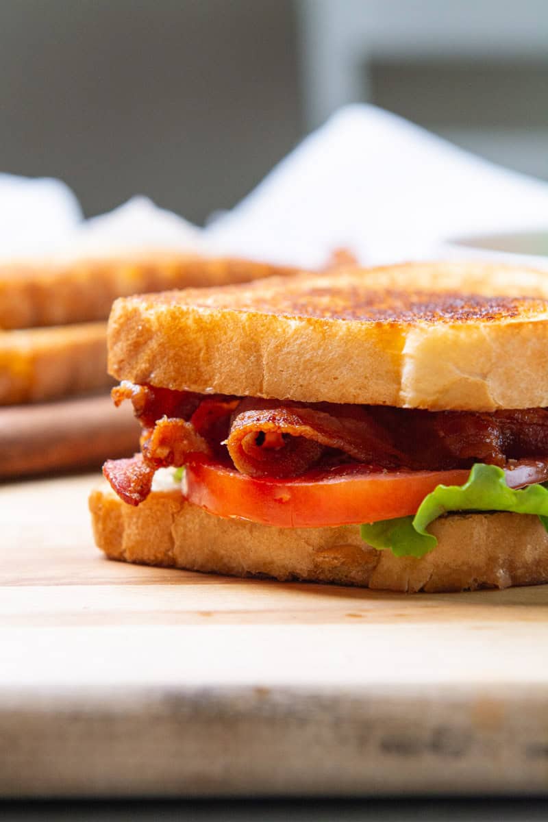 A BLT sandwich resting on a wooden cutting board.