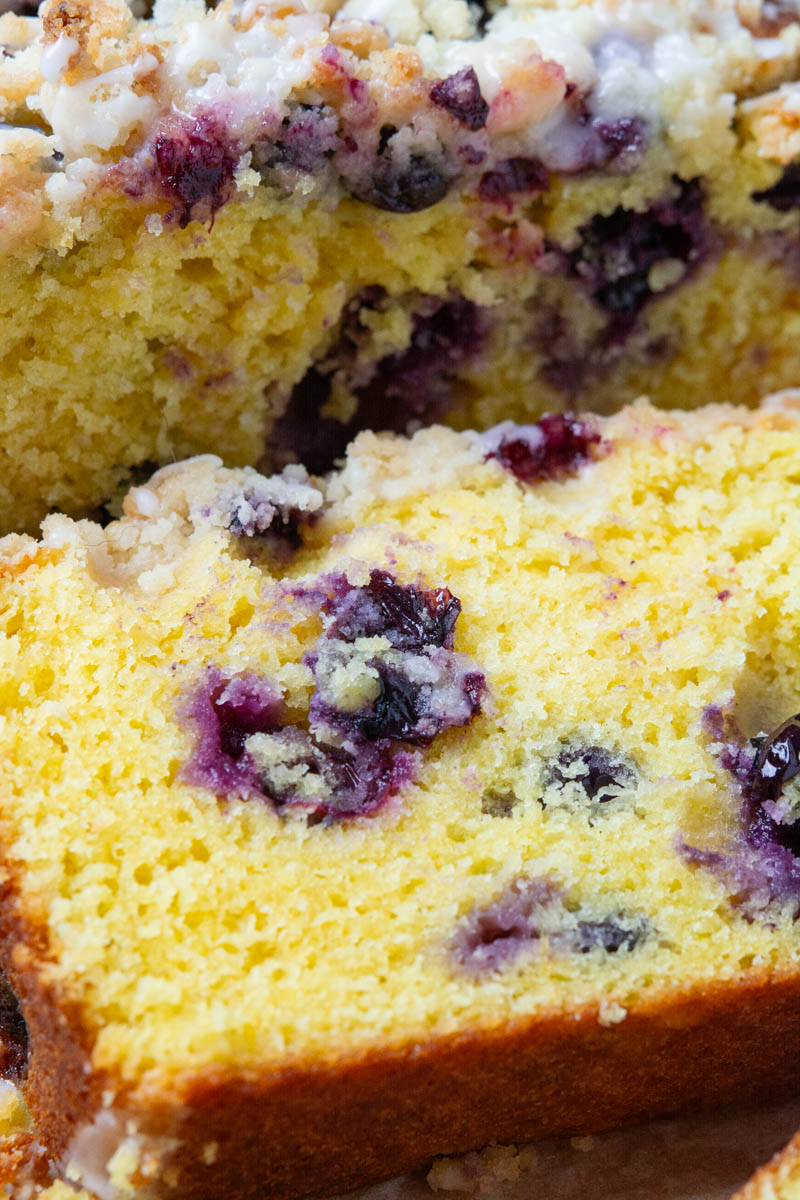 A slice of a lemon blueberry loaf topped with a delicious, golden brown crumble and drizzled with a sweet lemon icing.