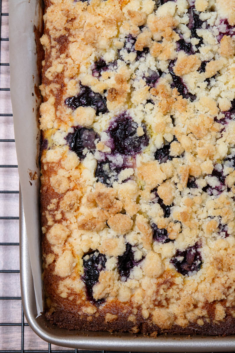 A loaf pan with a baked lemon blueberry loaf topped with a delicious, golden brown crumble.