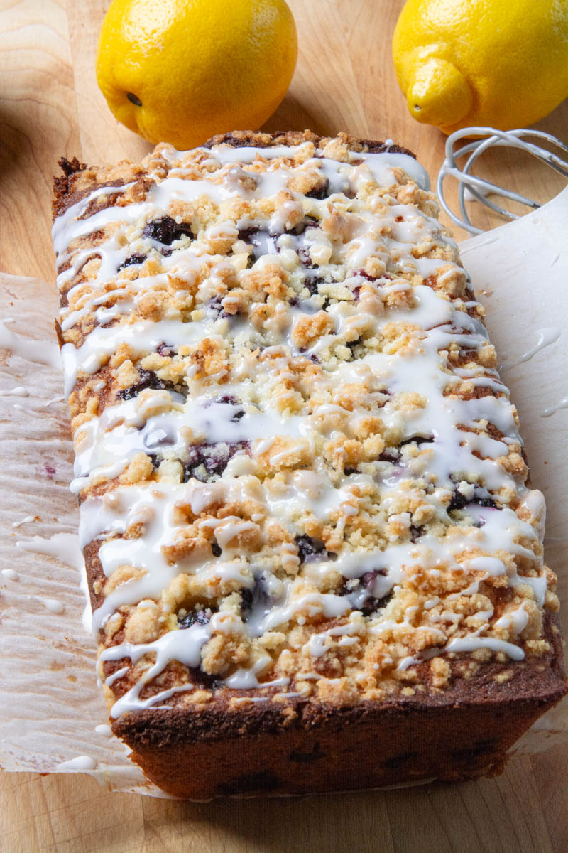 A baked lemon blueberry loaf topped with a delicious, golden brown crumble and drizzled with sweet lemon icing.