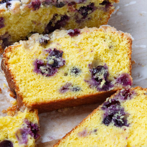 A slices of lemon blueberry loaf topped with a delicious, golden brown crumble and drizzled with a sweet lemon icing.