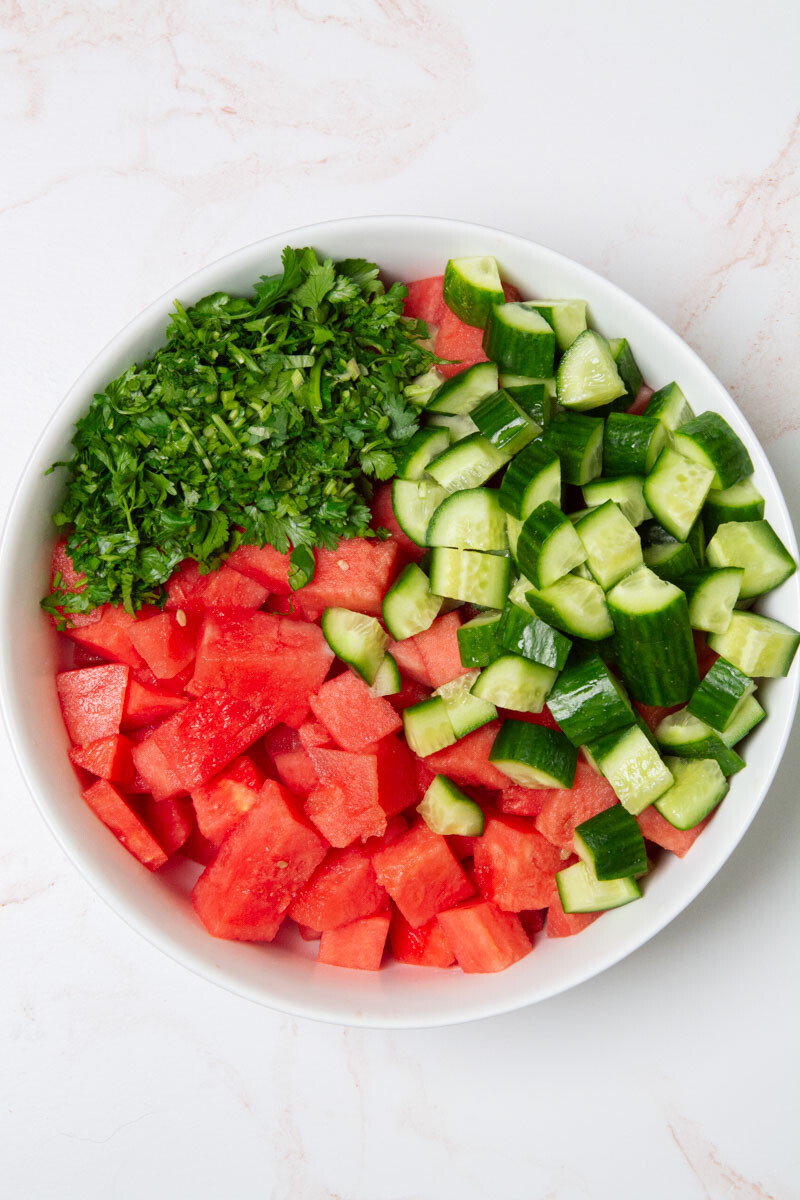 A large bowl with cubes of watermelon, cucumbers, and chopped cilantro for a watermelon cucumber salad