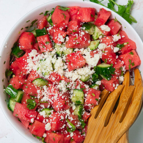 A large bowl with cubes of watermelon, cucumbers, chopped cilantro, and crumbled cotija cheese for a watermelon cucumber salad
