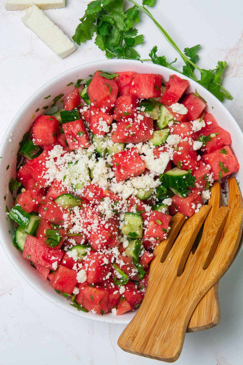 A large bowl with cubes of watermelon, cucumbers, chopped cilantro, and crumbled cotija cheese for a watermelon cucumber salad