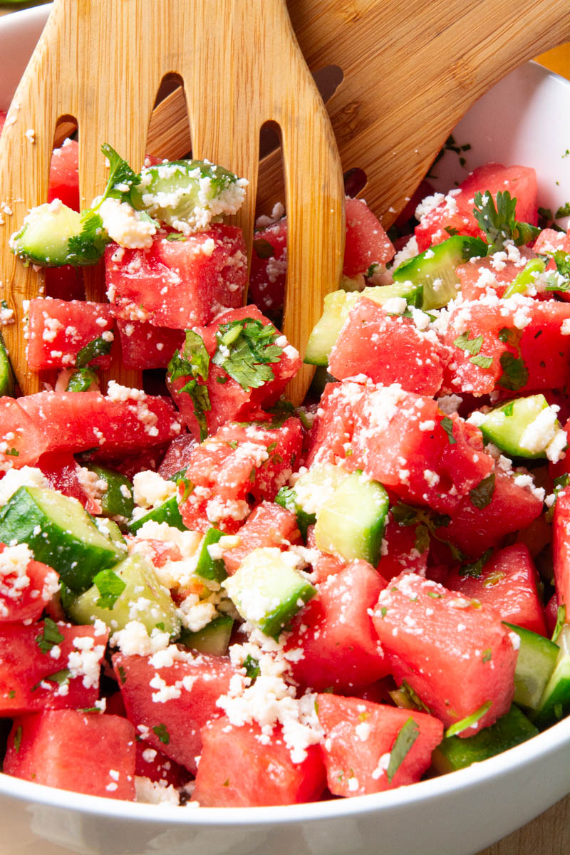 A large bowl with cubes of watermelon, cucumbers, chopped cilantro, and crumbled cotija cheese for a watermelon cucumber salad