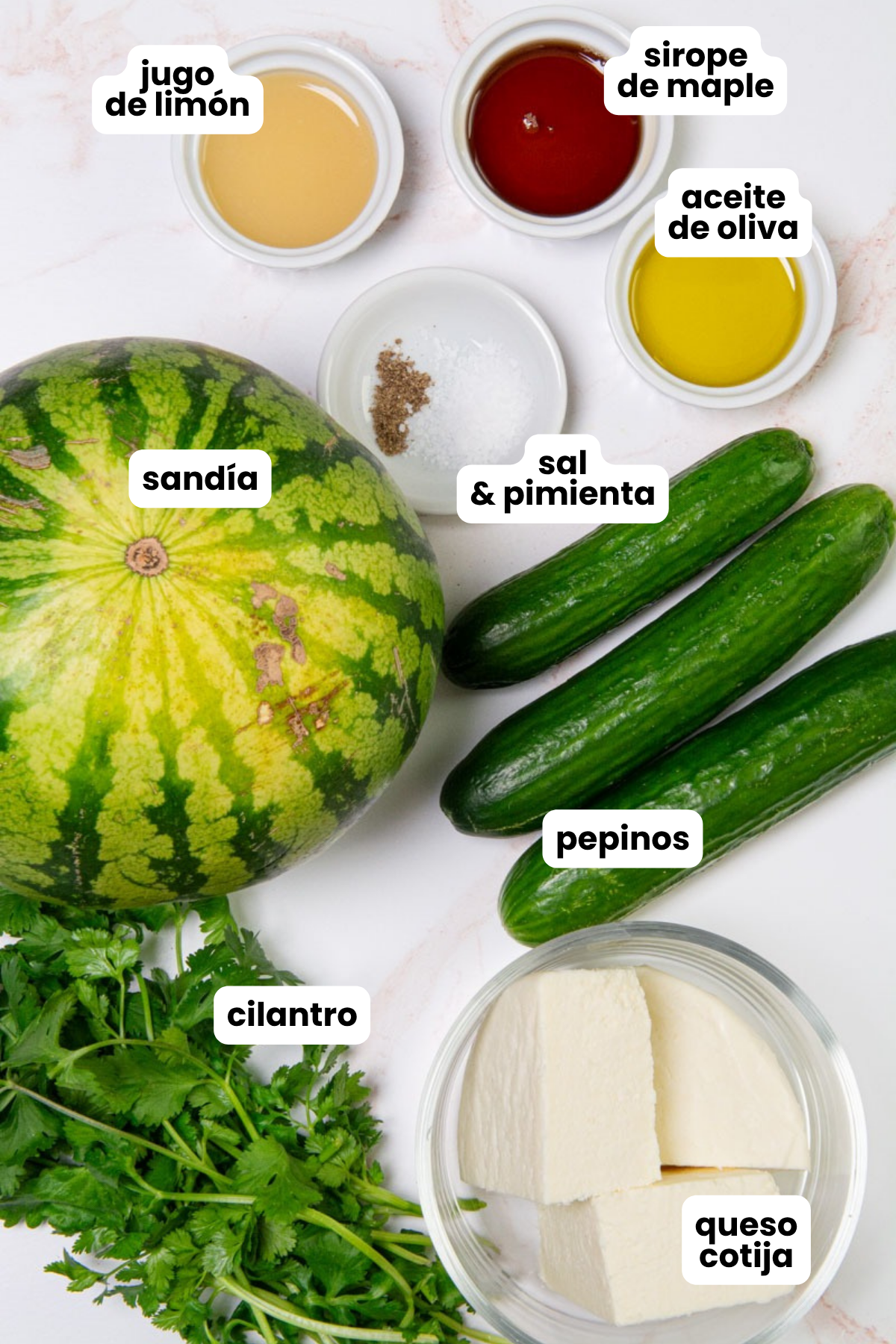 List of ingredients in Spanish for a watermelon cucumber salad which include watermelon, cucumbers, cilantro, cotija cheese, maple syrup, lime juice, olive oil, salt, and pepper.