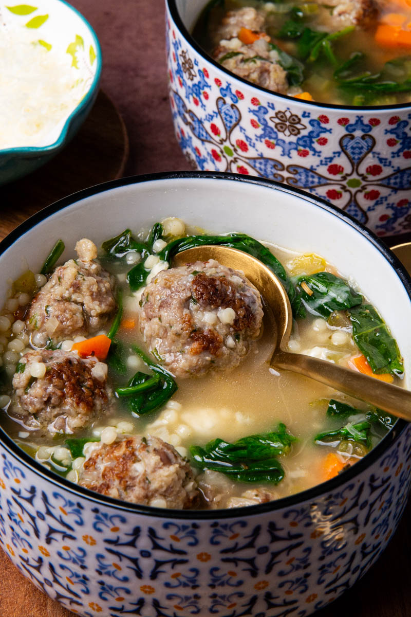 A bowl of Italian Wedding Soup with seared Italian meatballs, broth, spinach, onion, celery, carrots, and ancini di pepe pasta.