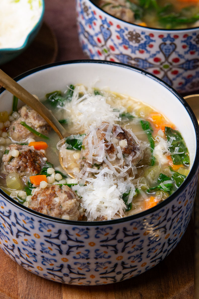 A spoonful of Italian Wedding Soup with seared Italian meatballs, broth, spinach, onion, celery, carrots, and ancini di pepe pasta all sprinkled with freshly grated Parmesan cheese.