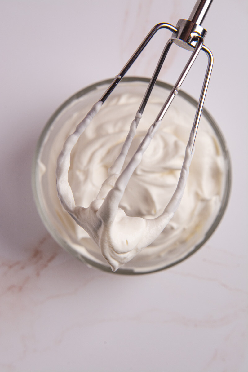 A bowl of fresh, homemade whipped cream and a whisk with whipped cream stiff peaks floating on top.