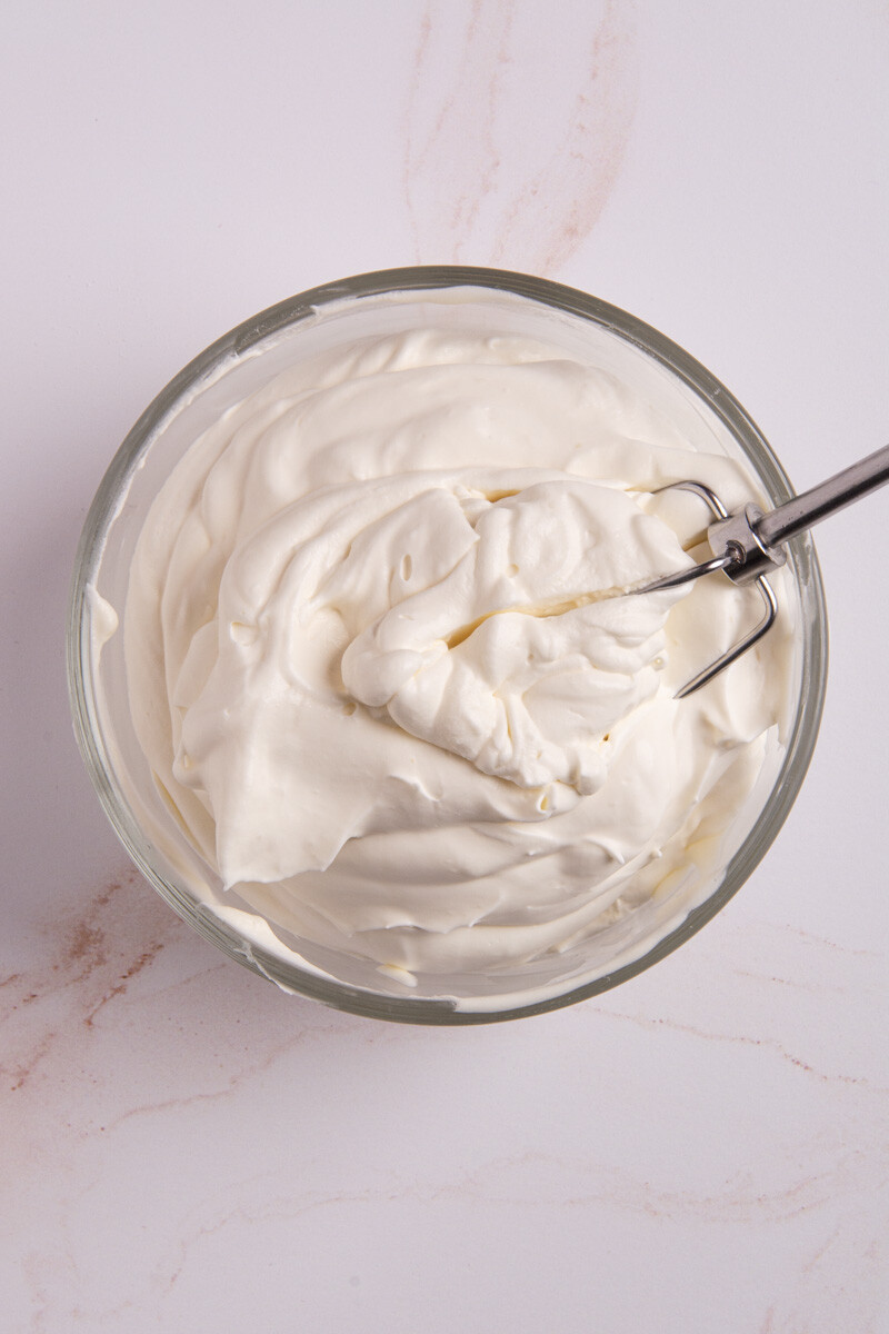 A bowl of fresh, homemade whipped cream with a whisk dipped in the fluffy center.