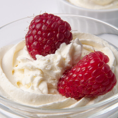 A bowl of fresh, homemade whipped cream with two raspberries on top.