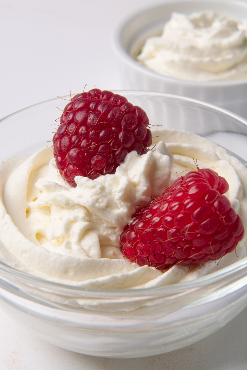A bowl of fresh, homemade whipped cream with two raspberries on top.