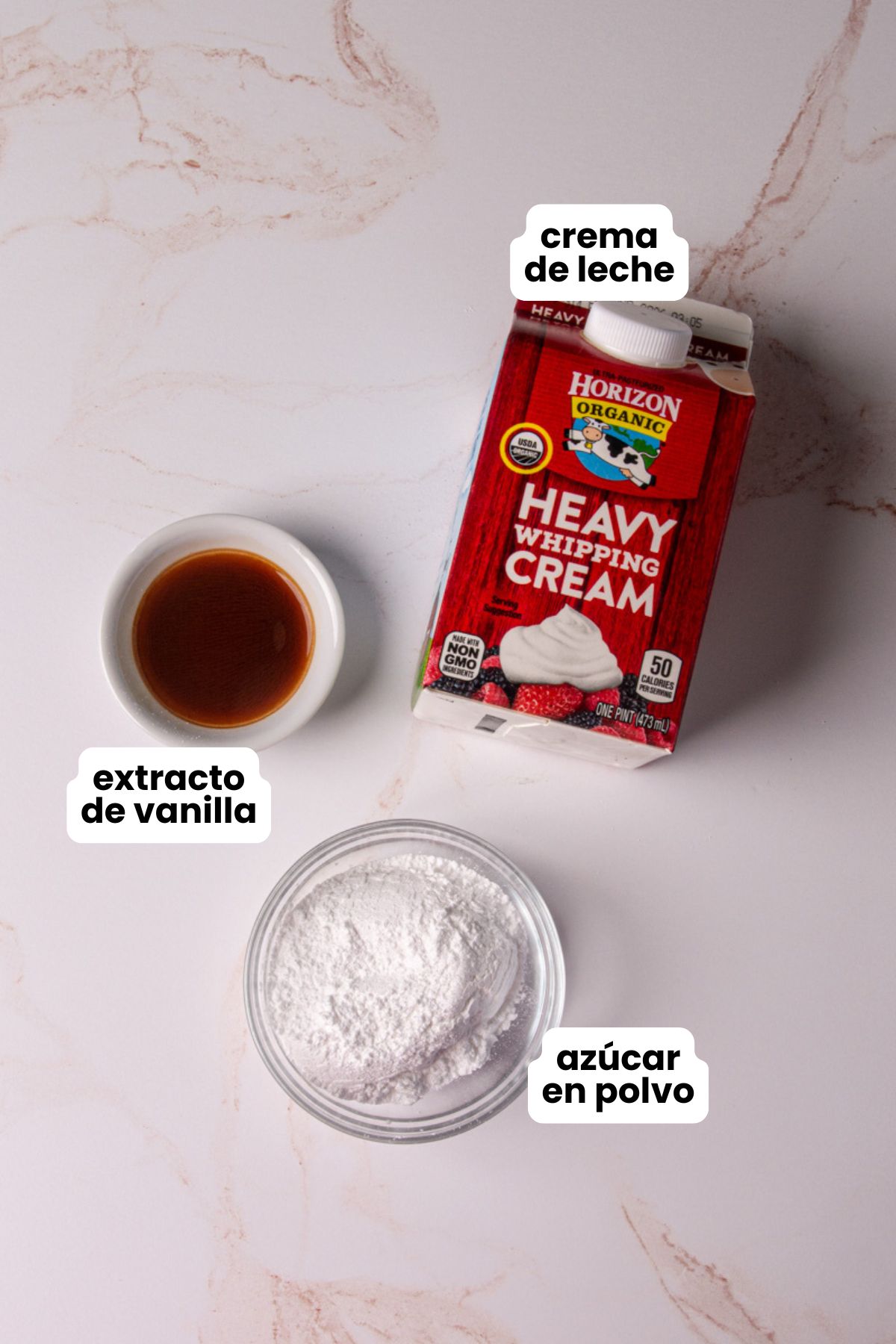 List of Ingredients for homemade whipped cream in Spanish which include heavy whipping cream, vanilla extract, and powdered sugar.