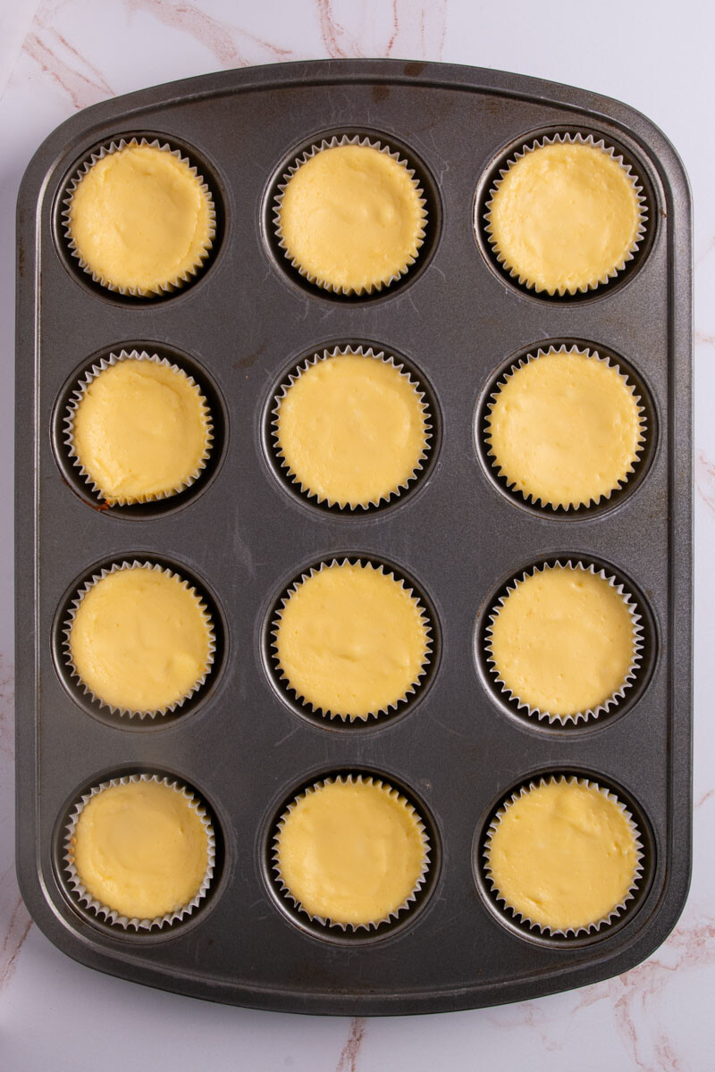 A cupcake tray with baked mini cheesecakes