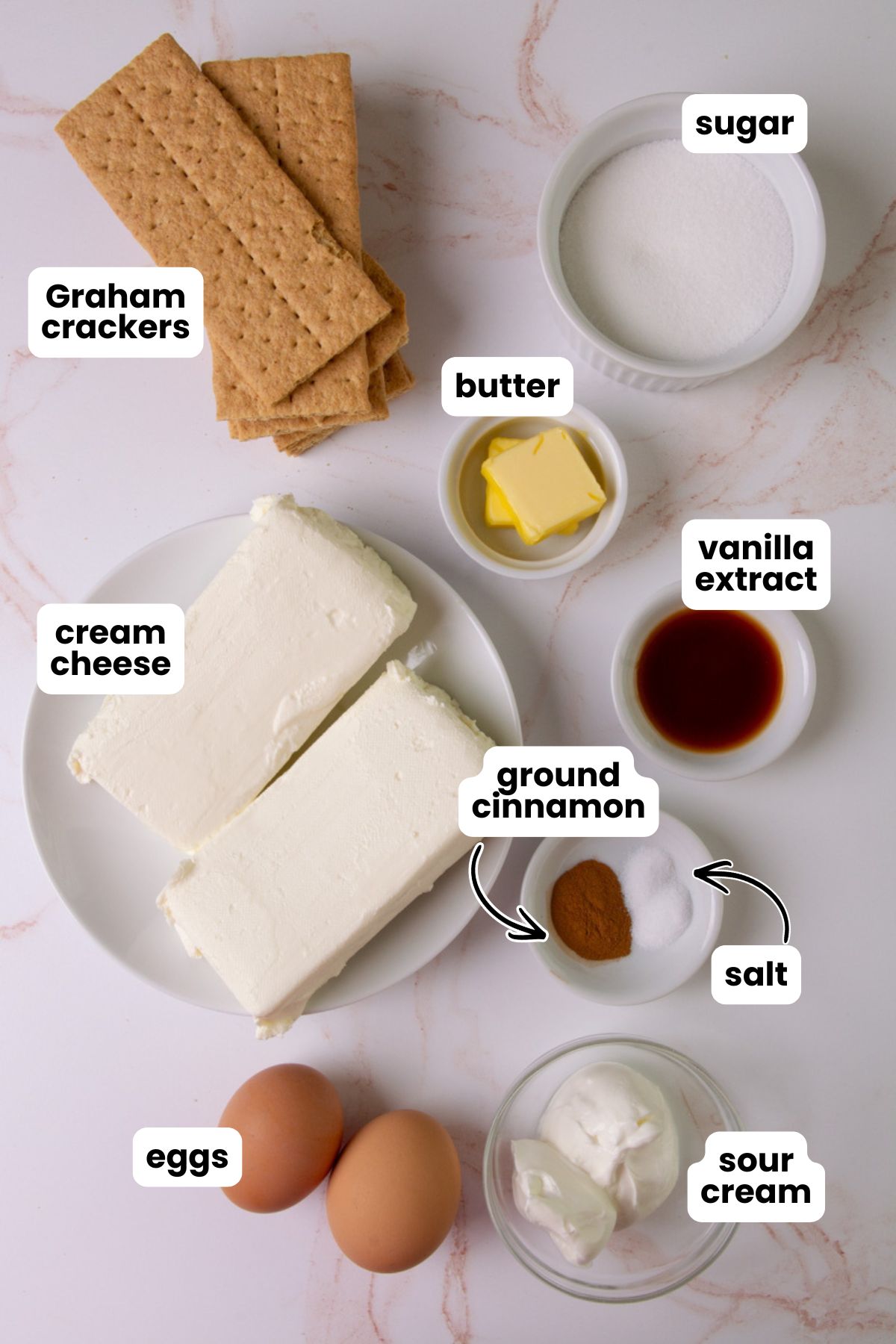 List of ingredients for making mini cheesecakes which include Graham crackers, white sugar, butter, cream cheese, sour cream, eggs, vanilla extract, ground cinnamon, and salt