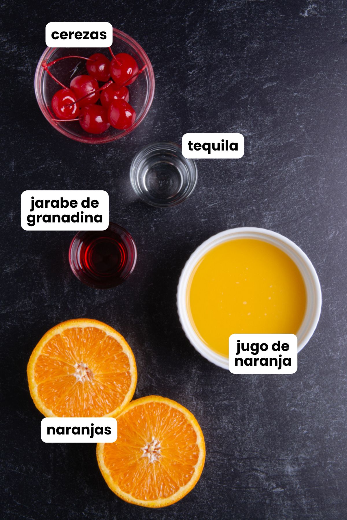Overhead flat lay of tequila sunrise ingredients on a dark surface: maraschino cherries, a shot of tequila, grenadine syrup, fresh orange juice, and halved oranges, each labeled in Spanish with text overlays.