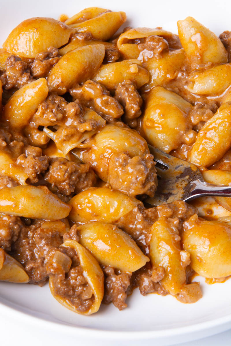Close-up of homemade hamburger helper with pasta shells and ground beef coated in a glossy, seasoned sauce, with a fork digging into the bowl.